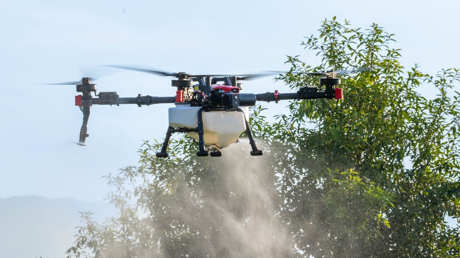 Drone spraying a field with trees in the background